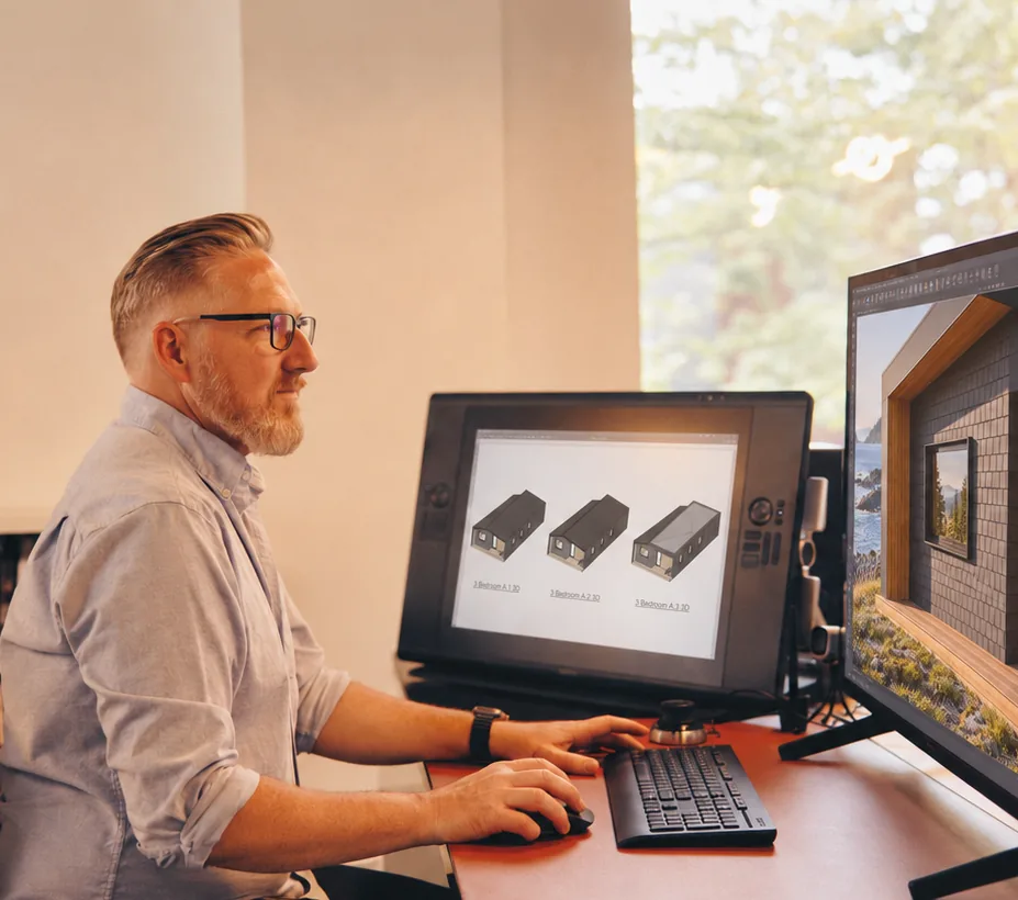 A Placemark designer at two screens, cabin models and an exterior render in progress